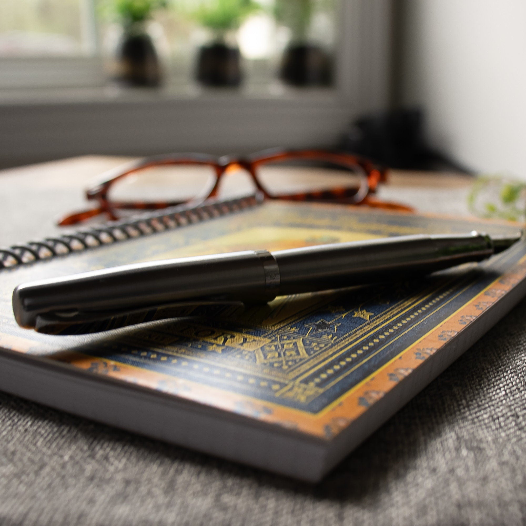 detail shot of a travel-sized notebook featuring a vintage book cover: Mary Howitt&#39;s Poems of Natural History for the Young. Features a framed illustration of two colorful parrots. Colors are deep blue, orange, gold and green.