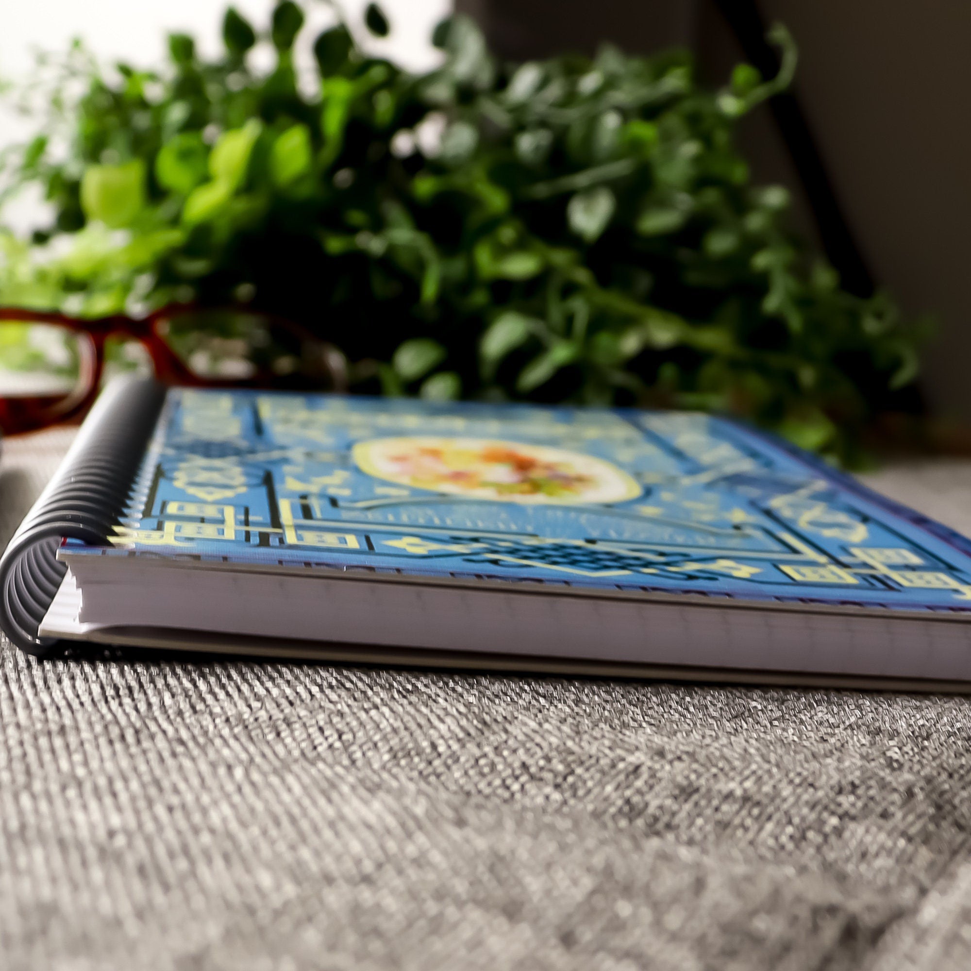 A travel-sized spiral notebook featuring a vintage book cover: Flora Symbolica or The Language and Sentiment of Flowers. Features a floral illustration surrounded by an ornate frame. The colors are sky blue, black, red, pink and gold.