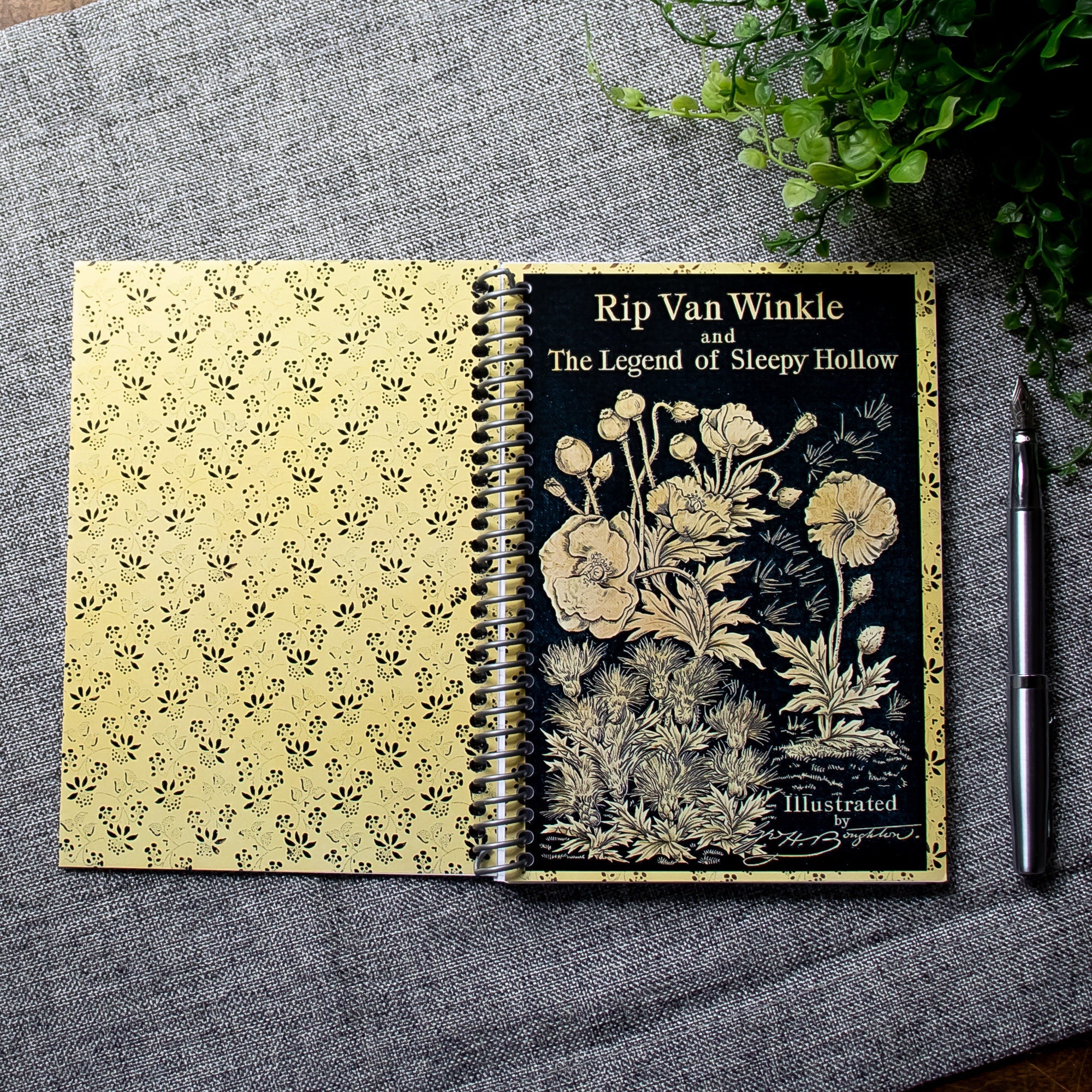 A travel-sized spiral notebook featuring a vintage book cover: Rip Van Winkle and The Legend of Sleepy Hollow by Washington Irving. Features a bold floral design. The colors are black and gold.